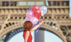 Femme en robe rouge tenant des talons devant la Tour Eifel